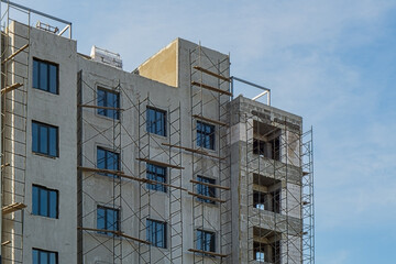 Multi-storey building under construction, erection of interior partitions from silicate bricks, installation of plastic windows, preparation of exterior for insulation, decoration using scaffolding