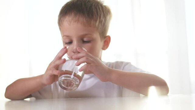 Boy drinks water from a glass in the kitchen. liquid healthy drink beverage concept. a boy drinks water from a glass. the boy drinks water and holds lifestyle a glass cup.