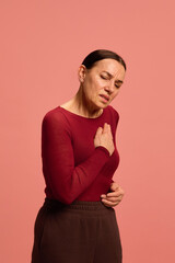 Obraz premium Elderly woman, pensioner clutches her chest in discomfort, portraying heart pain or shortness of breath against pink studio background. Concept of healthcare, medicine, infection and treatment. Ad.