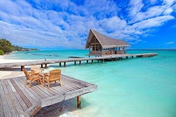 Tropical overwater bungalow with wooden deck turquoise ocean and scenic blue sky