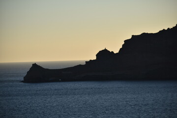 Rocky coastline silhouette at sunrise with a calm sea and soft light The early morning scene captures the natural beauty of the ocean horizon and rugged cliffs in peaceful solitude