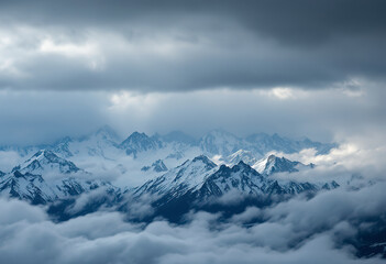 Dramatic aerial view to large snow mountain range under changeable rainy cloudy sky. Bright atmospheric alpine scenery with high snowy mountain peak in low clouds.