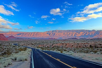 Desert road leading to rocky mountains under bright blue sky and sunny weather