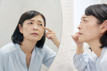 鏡で目尻を見て悩む50代女性