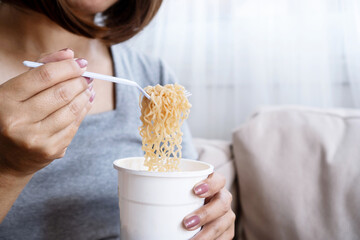 close-up of a woman's hand eating noodles from a plastic cup, unhealthy fast food habit