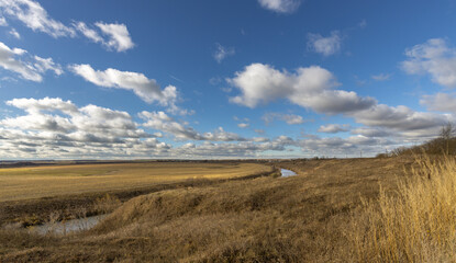 Obraz premium A field with a river running through it and a cloudy sky