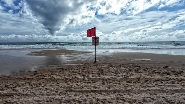 A red no swimming flag blowing in the wind on Mermaid beach warning of dangerous rip current