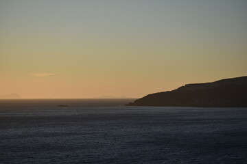 A tranquil seascape at dusk with a glowing golden horizon, distant islands, and calm waters, creating a peaceful and serene atmosphere with the beauty of nature on full display
