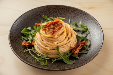 a plate of pasta, beautifully twirled and served on a dark, speckled plate