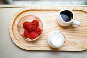 Strawberry ice cubes with a jar of milk and a cup of espresso on a wooden tray. Preparation for making strawberry latte.