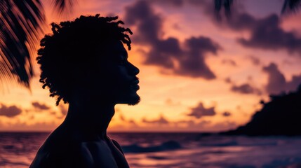 Man's silhouette against a vibrant sunset sky on a tranquil beach with palm trees creating a serene and picturesque atmosphere