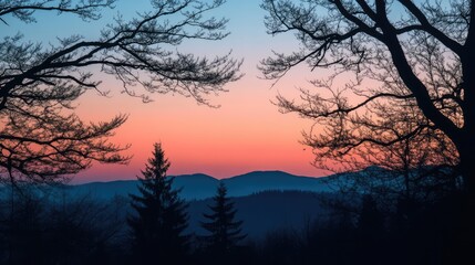 Obraz premium Serene silhouette of trees framing a colorful sunset over distant mountains and a calm sky in twilight hues.