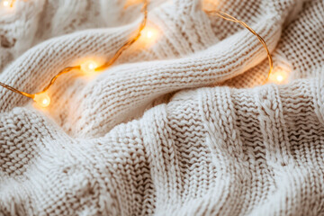 Fototapeta premium Close-up of a creamy knitted sweater, yarn, with warm string lights, radiating cozy winter vibes. Festive mockup for lifestyle, hygge-inspired designs. Generative ai 