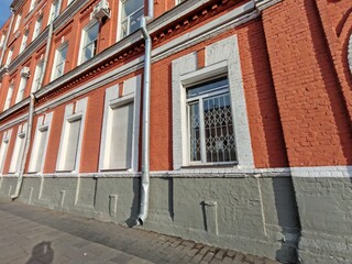 A sturdy metal downspout attached to a textured red brick facade with white window trims. The photo captures construction materials and the importance of drainage systems in urban building