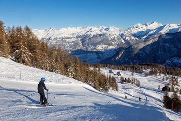 Pistes de ski dans les Alpes, en Valais, Suisse. Montagnes enneigées, skieurs et forêt de mélèzes.