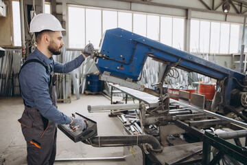 Factory worker operating industrial cutting machine for aluminum and PVC windows and doors...