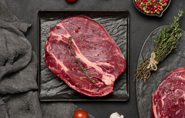 Raw chuck eye roll beef steak on black board, peppercorns, and sprigs of thyme, viewe from above
