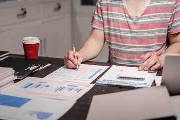 A man sits at his desk at home at night, working on his laptop. He views charts, checks documents,...
