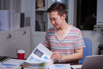 A man sits at his desk at home at night, working on his laptop. He views charts, checks documents, and analyzes financial data, focusing on investments, stock trading, and shareholder rights