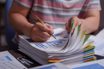 A man sits at his desk at home at night, working on his laptop. He views charts, checks documents,...