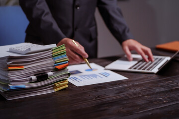 A man sits at his desk at home at night, working on his laptop. He views charts, checks documents,...
