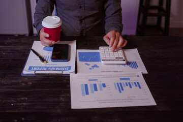 A close-up of a male businessman at his desk, analyzing overtime graphs and business charts in a...