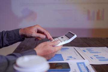 A close-up of a male businessman at his desk, analyzing overtime graphs and business charts in a...