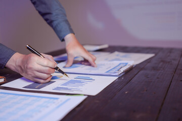A close-up of a male businessman at his desk, analyzing overtime graphs and business charts in a...