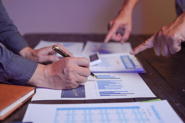 A close-up of a male businessman at his desk, analyzing overtime graphs and business charts in a...