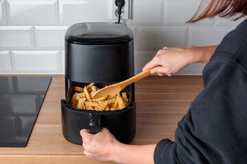Woman at home using trendy kitchen gadget air fryer machine cooking deep-fried potato, small...