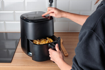 Woman at home using trendy kitchen gadget, deep fryer, selecting program on small convection oven...
