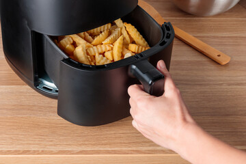 Woman at home using trendy kitchen gadget air fryer machine cooking deep-fried potato, small...