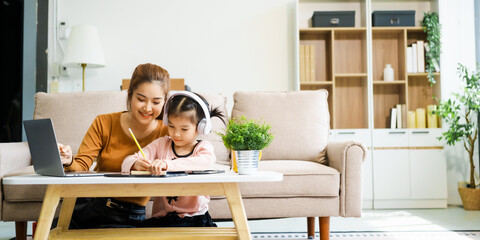 An Asian mother and her adorable daughter sit on the sofa in their living room, enjoying online...