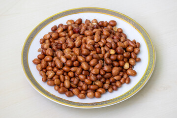 Spicy roasted peanuts in a white plate on a wooden surface.