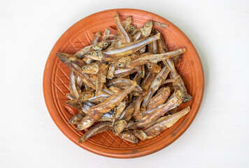 Dried anchovy fish (Mola Shutki in Bangladesh) on a clay plate, isolated on a white background.