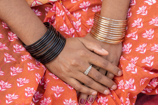 Close-up of a beautiful Bengali woman's hands adorned with colorful glass bangles, a ring, and nail polish.