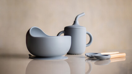 Silicone baby tableware set in gray, the first soft cup for toddlers. Baby eating utensils. Nutrition and feeding concept