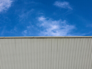 Industrial factory building with aluminum metal texture on the exterior wall against the background of blue sky and clouds, modern architecture of corrugated steel facade. Copyspace, design.