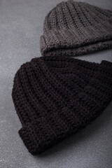 Two knitted woolen beanie caps or hats, black and grey on wooden background.