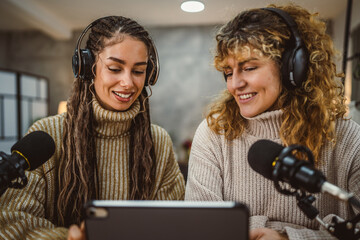 Two young adult women stream audio podcast use microphone and tablet