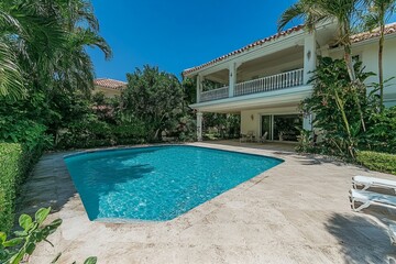 A tropical villa surrounded by lush palm trees, with a swimming pool and an open-air living area