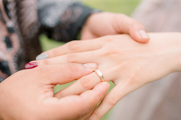 Wedding rings on the hands of the newlyweds, a bouquet of flowers in the background.