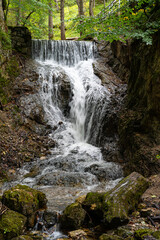 Rocky waterfall and large boulders covered with moss in the foreground