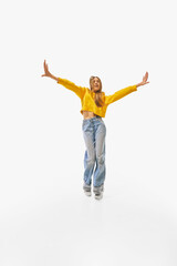 Woman in vibrant yellow sweater and casual blue jeans standing confidently with arms stretched wide and relaxed posture against white studio background. Concept of success, professional, movement. Ad