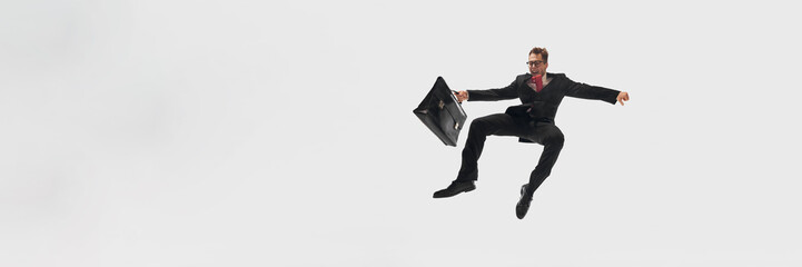 Banner. Businessman in black suit and red tie mid-air, holding black briefcase flying against white studio background with copy space. Concept of success, professional development, movement. Ad