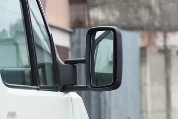 one big black plastic car mirror next to the gray glass of a white auto on the street