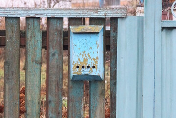 one blue old metal mailbox hanging on gray wooden planks of fence wall in the street