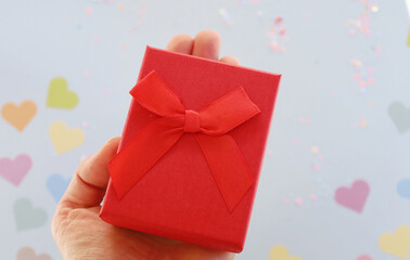 red gift on hand on background of hearts
