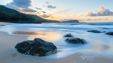 Stunning long exposure of rocks on the beach at dawn with softly flowing waves and serene sky in the background.