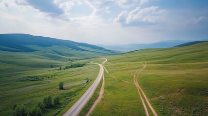 Fototapeta premium Aerial view of winding roads through green agricultural fields under a blue sky in a serene summer landscape with gentle hills.